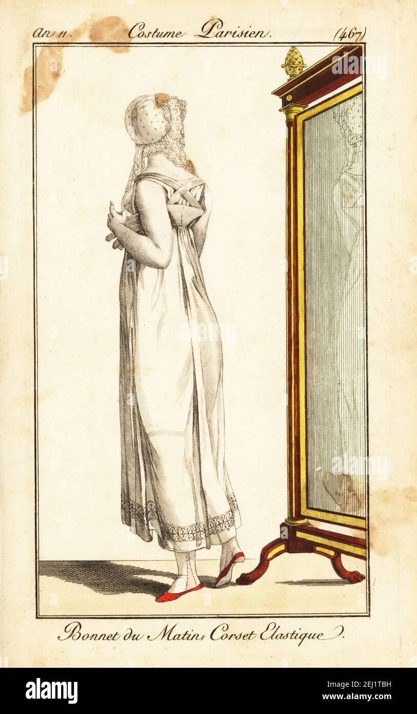 Merveilleuse vor einem Spiegel. Sie trägt eine Morgenhaube aus Spitze, ein durchsehbares Musselin-Kleid mit einem elastischen Korsett. Bonnet du Matin, Korsett Elastique. Handkolorierter Kupferstich aus Pierre de la Mesangeres Journal des Dames et des Modes, Magazine of Women and Fashion, Paris, an 11, 1803. Illustrationen von Carle Vernet, Jean-Francois Bosio, Dominique Bosio und Philibert Louis Debucourt, gestochen von Pierre-Charles Baquoy. Stockfoto