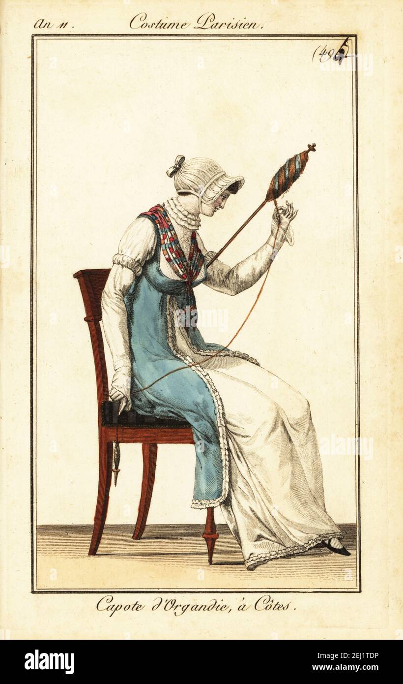 Frau Spinngarn mit Spindel und Stab, Paris, 1803. Sie trägt eine Kapuzenmütze in gerippter Organdy, blauer Tunika über einem weißen Kleid, gekräuselten Kragen und Fichu. Capote d’Organdie, à Côtes. Handkolorierter Kupferstich aus Pierre de la Mesangeres Journal des Dames et des Modes, Magazine of Women and Fashion, Paris, an 11, 1803. Illustrationen von Carle Vernet, Jean-Francois Bosio, Dominique Bosio und Philibert Louis Debucourt, gestochen von Pierre-Charles Baquoy. Stockfoto