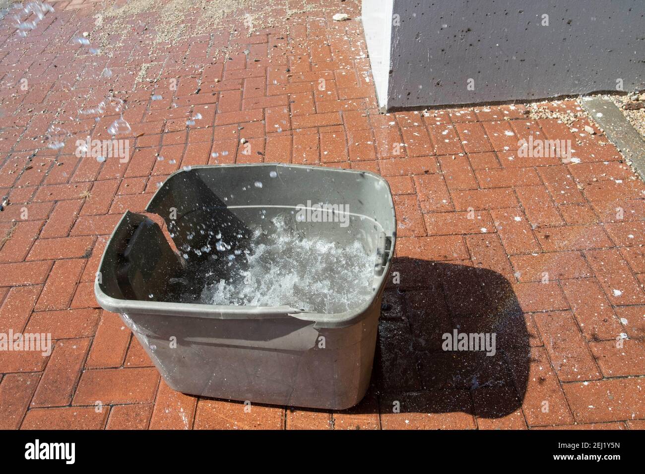 Austin, Texas USA 20. Februar 2021: Ein großer Plastikbehälter wird aufgestellt, um Wasser vom schmelzenden Schnee zu fangen, der von einem erhöhten Abschnitt des US Highway 183 in Nord-Austin tropft, an der Stelle eines Obdachlosenlagers, in dem fast ein Dutzend Menschen untergebracht sind. Viele Bewohner flüchteten während der Rekordkälte und des Schneefalls in wärmende Schutzräume, kehrten aber in das Lager zurück, als die Temperaturen über das Wochenende anstiegen. Kredit: Bob Daemmrich/Alamy Live Nachrichten Stockfoto