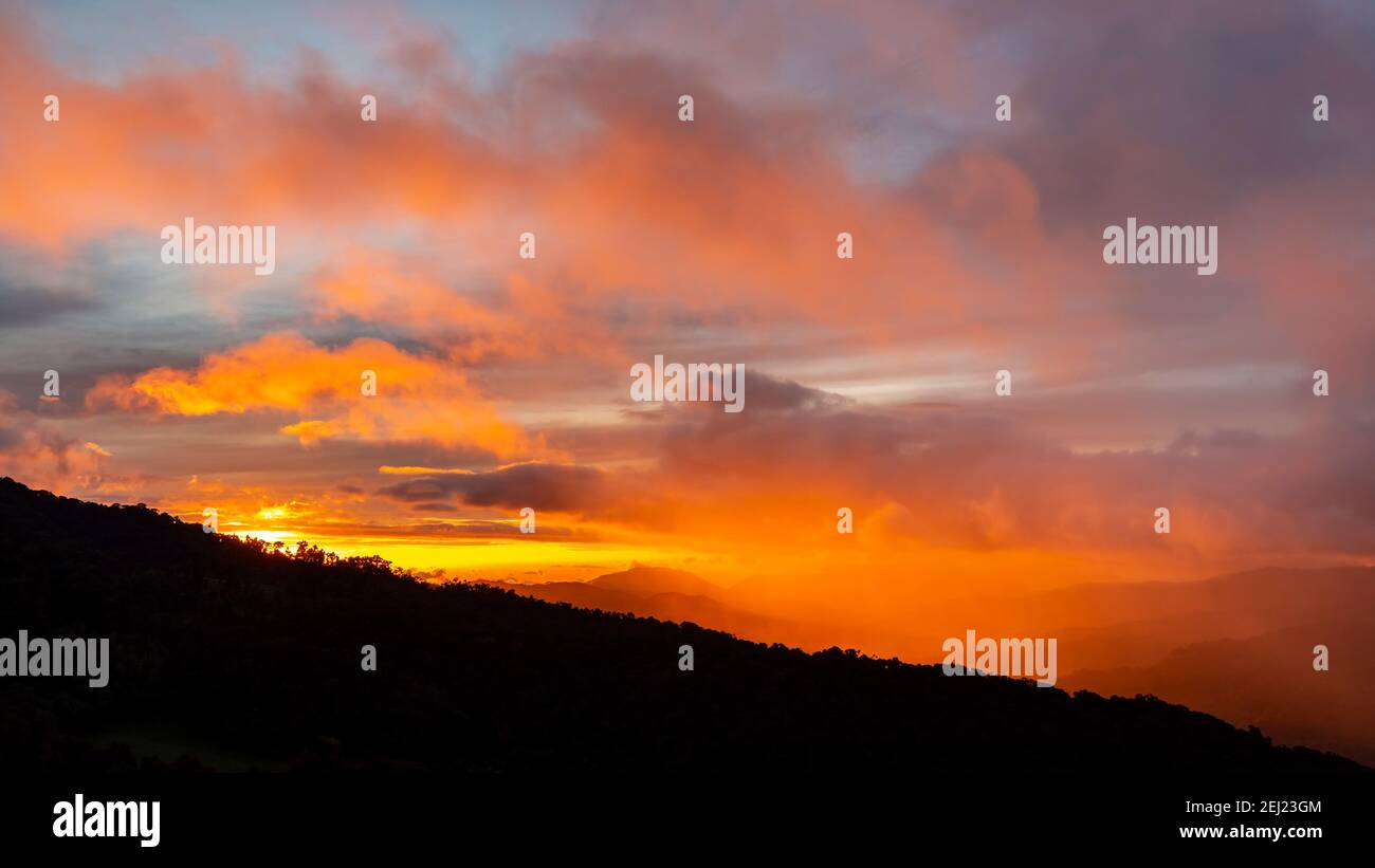 Hoher Aussichtspunkt eines intensiven orangen Sonnenuntergangs mit Wolken und Regen im Nebelwald, Dota, Costa Rica Hochland Stockfoto