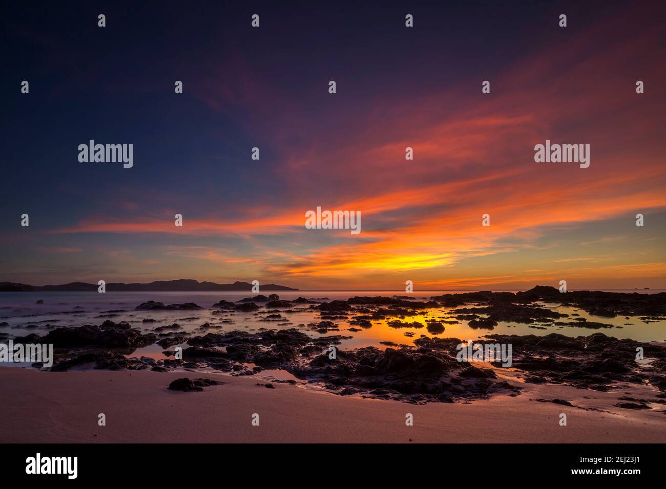 Tropischer Sommer Sonnenuntergang Landschaft am Strand mit Sand, Felsen, Wasser, ruhiges Meer, bunter blauer Himmel mit orangen Wolken, Guanacaste, Costa Rica Stockfoto