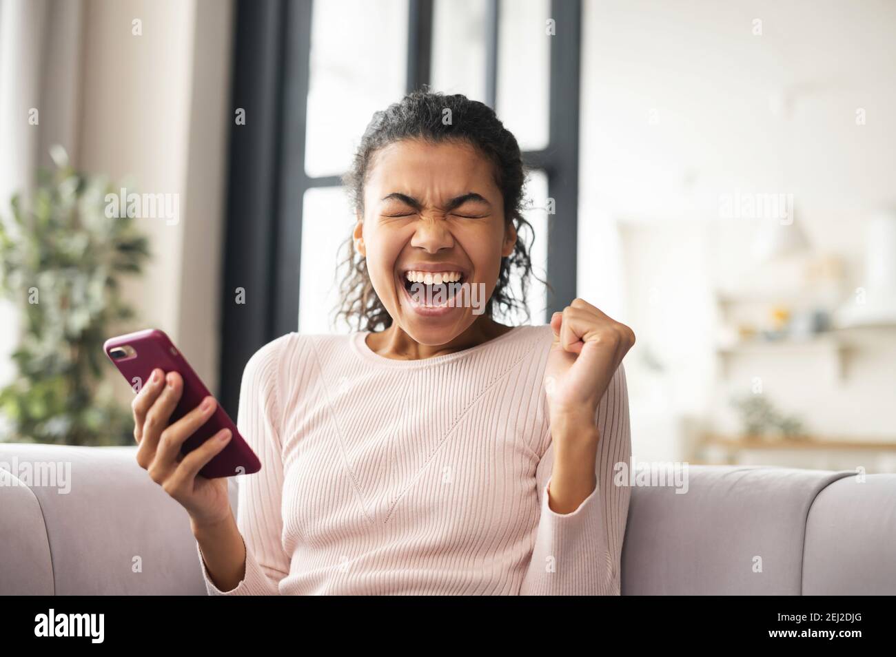 Afroamerikanische schöne Frau ist überrascht, was sie am Telefon sah, bekam Nachricht, bestand die Prüfung erfolgreich, eingestellt, bekam ein Visum, begeistert von Stockfoto