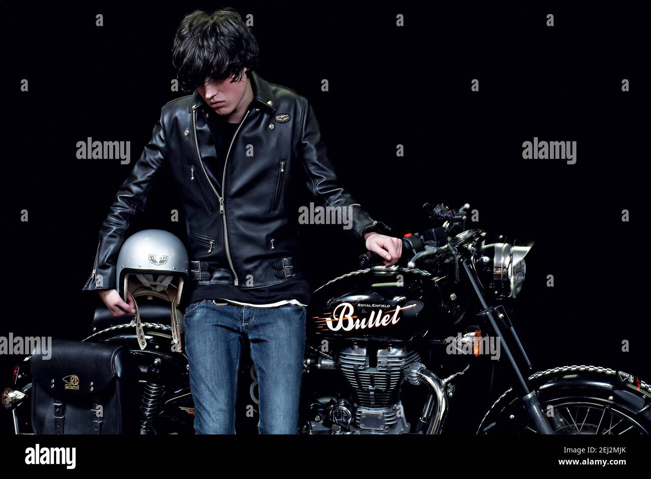 Junger Biker in schwarzer Lederjacke mit Motorrad im klassischen Stil und schwarzem Hintergrund.männlicher Biker innen mit Cafe Racer. Stockfoto