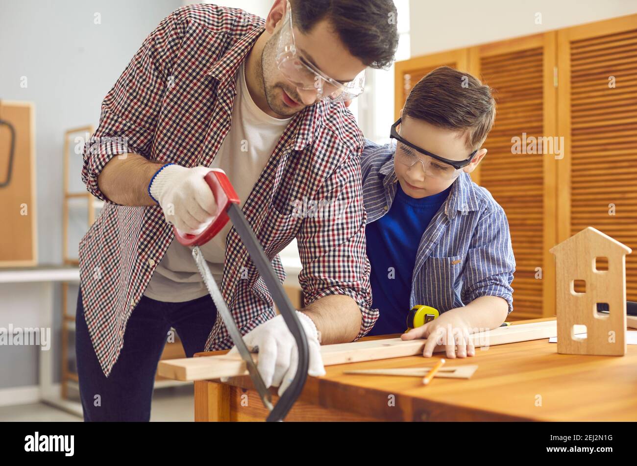 Papa lehrt seinen kleinen interessierten Sohn, in der Werkstatt ein Holzspielzeughaus zu bauen. Stockfoto
