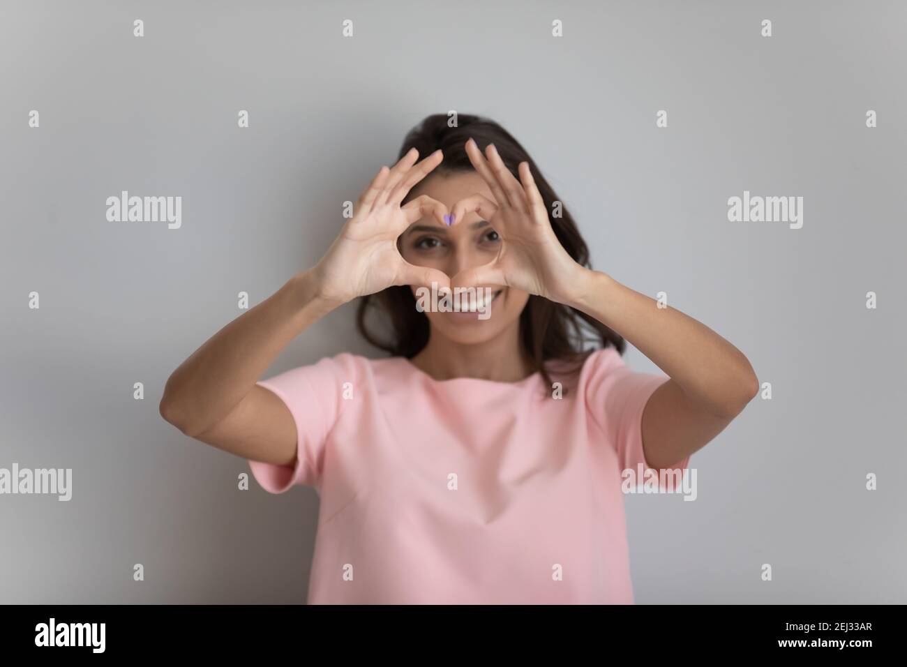 Positive arabische Frau, die durch das Fingerherz auf die Kamera schaut Stockfoto