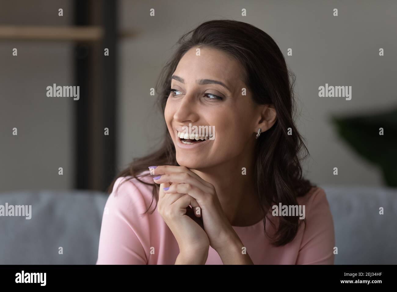 Positive indische arabische Frau sitzt auf dem Sofa lachend und schaut zur Seite Stockfoto