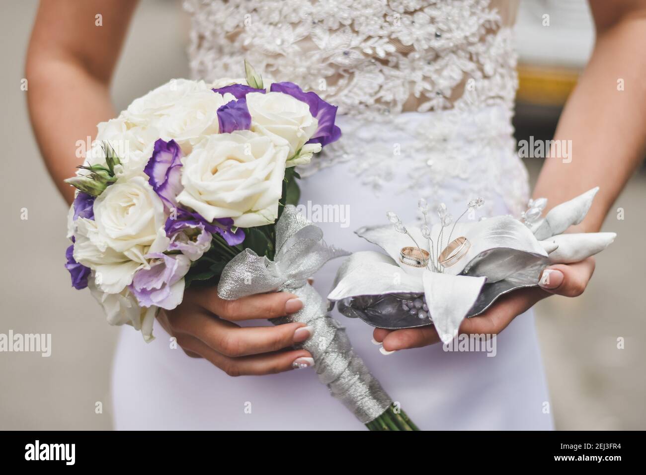 Die Braut hält einen Blumenstrauß und zwei Eheringe. Stockfoto