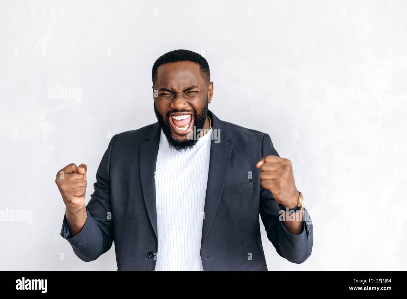 Emotional aufgeregt afroamerikanischen männlichen Unternehmer, Freiberufler oder Student in stilvollen Anzug, stehen auf isolierten Hintergrund, glücklich zu gewinnen oder unerwartete Nachrichten Stockfoto
