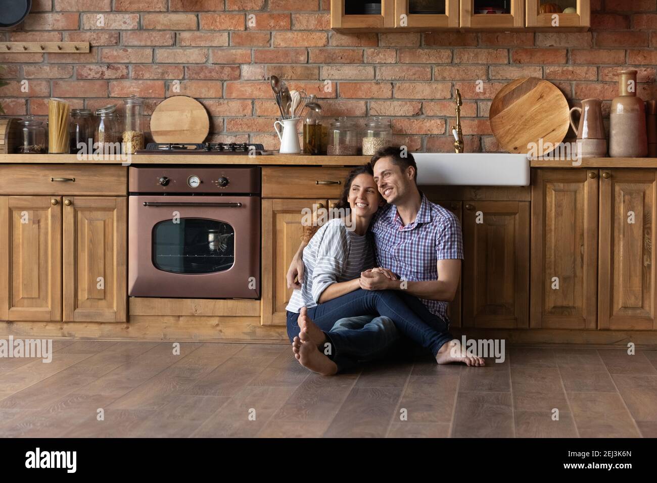 Lächelnder, verträumter Mann und Frau umarmen sich und sitzen auf dem Boden Stockfoto