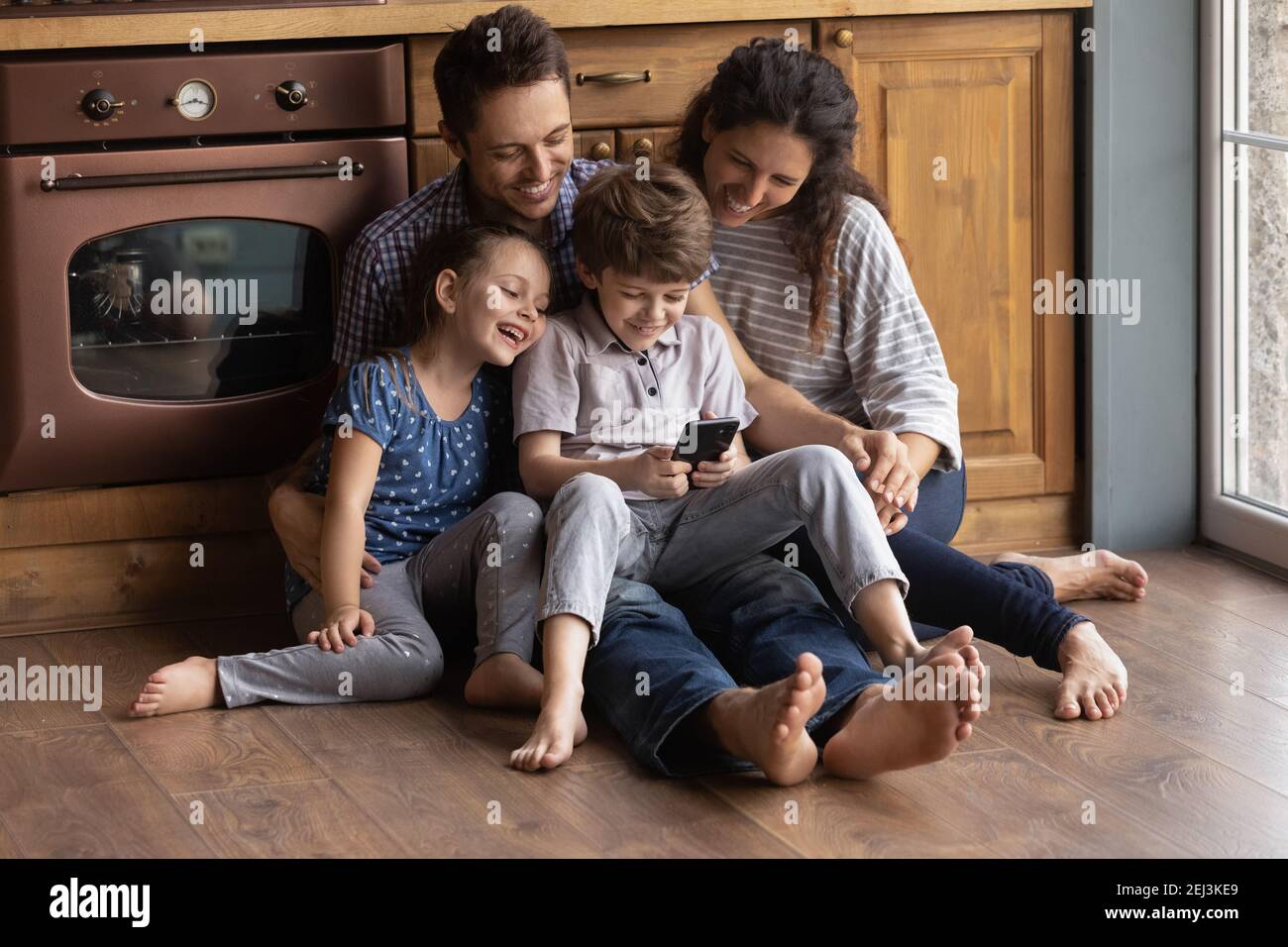 Glückliche Familie mit zwei Kindern, die telefonieren und auf dem Boden sitzen Stockfoto