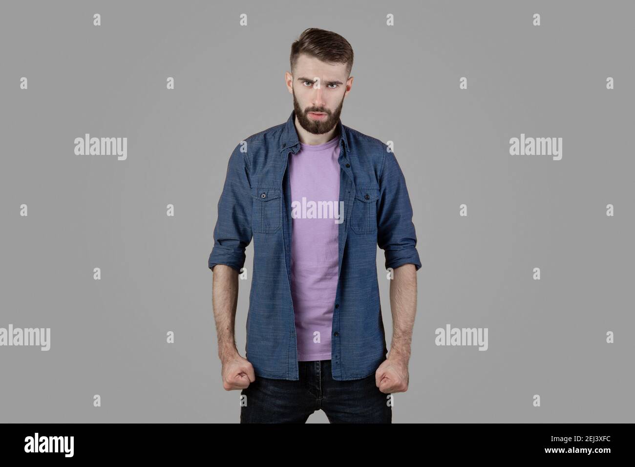 Wütender junger Mann, der seine Fäuste zusammenhält und seine Wut auf grauem Studiohintergrund unterdrückt. Konzept der negativen Emotionen Stockfoto