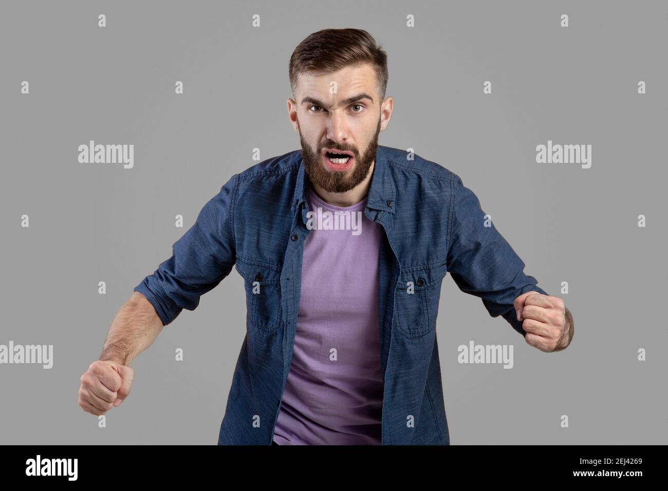 Portrait eines jungen wütenden Mannes, der vor Wut schreit, Fäuste auf grauem Studiohintergrund zusammenhält Stockfoto