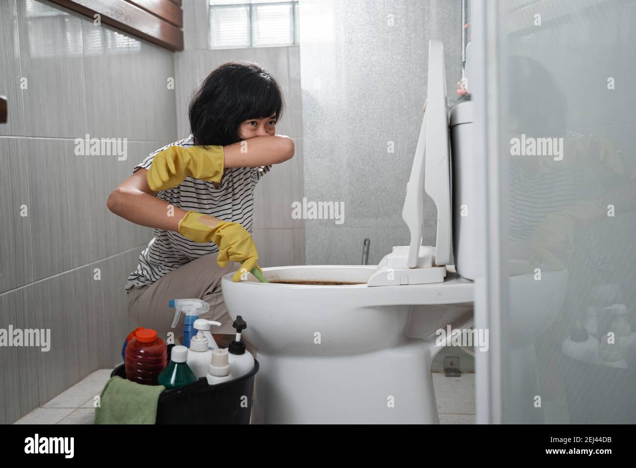 Hausfrau tragen Handschuhe über ihre Nasen, um stinkende Toilette zu reinigen Im Badezimmer Stockfoto