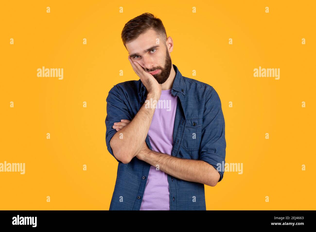 Porträt von gelangweilten kaukasischen Kerl lehnt auf der Handfläche und suchen Bei der Kamera auf orangefarbenem Studiohintergrund Stockfoto