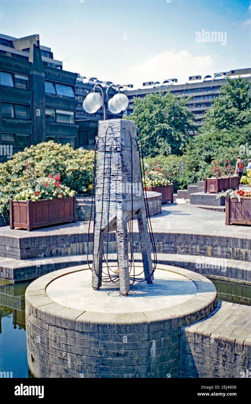 Eine Skulptur, die im Barbican Centre, London, England, UK 1993 installiert wurde. Dieses Stück trägt den Titel ‘You Fill my Head’ und ist von dem Künstler Tom Yuill. Sie befindet sich über einem Wasserbrunnen – vermutlich, als ein Ventil eingeschaltet wurde, bildete die Skulptur ein Wasserspiel. Dies war Teil der ‘Art in the City’ von 1993 und zielte darauf ab, Skulpturen zwischen den Grünflächen und der unverwechselbaren Architektur der City of London zu setzen. Ein ähnliches Schema, ‘Sculpture in the City’, begann 2011 mit Kunstwerken international anerkannter und aufstrebender Künstler, die jeden Sommer zu sehen waren – ein Vintage-Foto aus den 1990er Jahren. Stockfoto