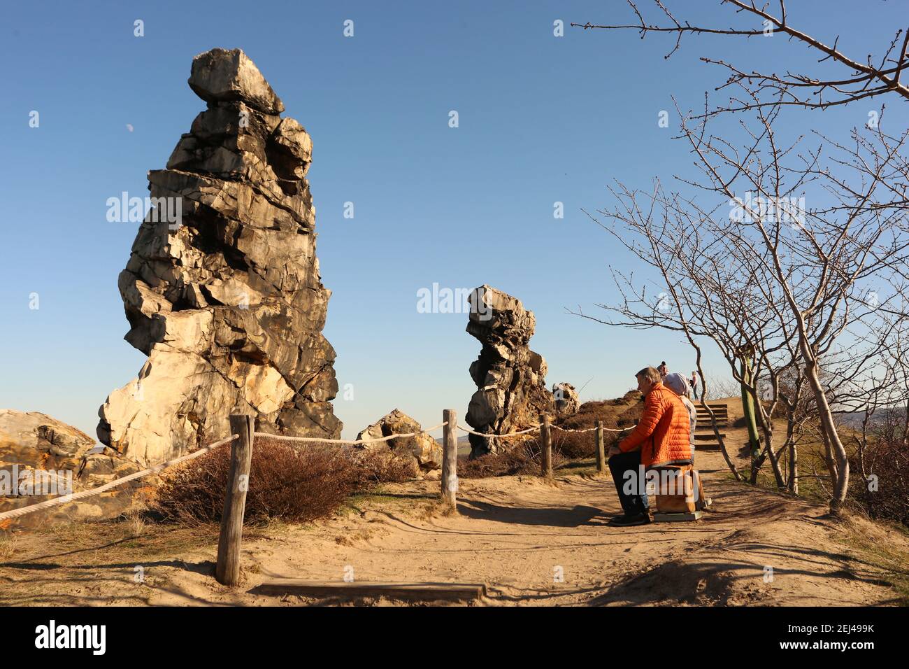 Thale, Deutschland. Februar 2021, 21st. Ausflügler sitzen auf einer Bank am Teufelsmauer. Die Felsen des Teufelsmauer, zwischen Blankenburg und Ballenstedt am Fuße des Harzes gelegen, sind ein Mini-Berg aus Sandstein. Es steht seit 1833 unter Naturschutz. Viele nutzten die frühlingshaften Temperaturen am Wochenende für einen Ausflug in den Harz. Quelle: Matthias Bein/dpa-Zentralbild/dpa/Alamy Live News Stockfoto