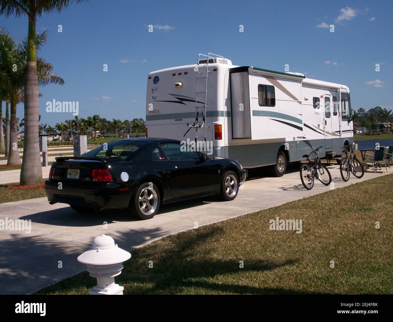 Wohnmobil parkt in einem modernen Wohnmobil-Resort in sonnigem, warmem Klima. Schwarzes Auto parkte hinter dem Wohnmobil in der Nähe von Fahrrädern. Stockfoto