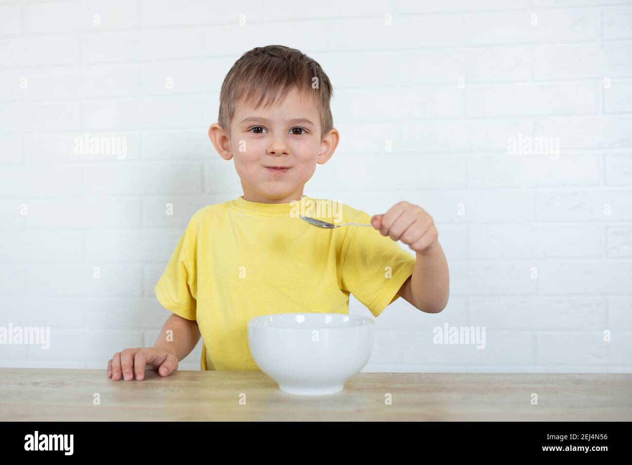 Kleiner Linkshänder Junge in einem gelben T-Shirt essen Obstsalat und lächeln. Kinder gesunde Ernährung Konzept. Ernährungsprodukte. Gesundheitswesen Stockfoto