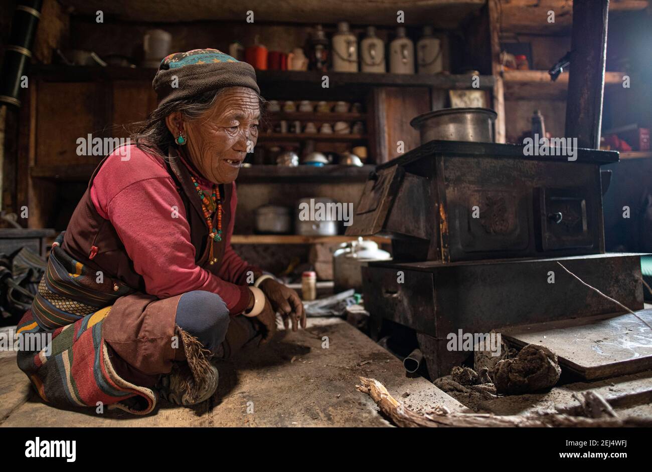Eine ältere Frau, die vor einem kleinen Herd in ihrer Küche sitzt, Tsakhang Gompa, Dolpo, Nepal Stockfoto