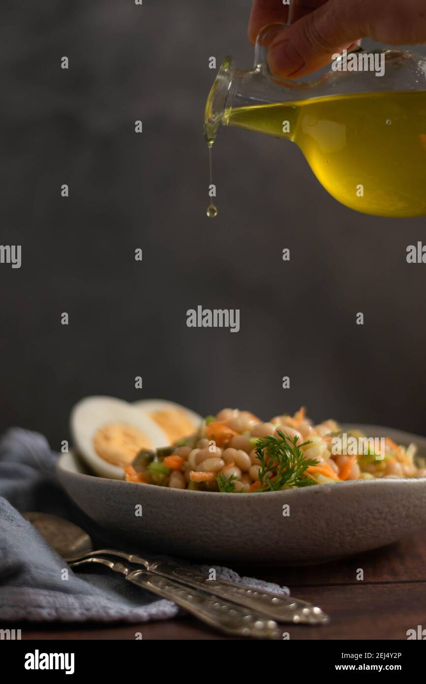 Gießen von Olivenöl auf Bohnen Salat. Gesunde Ernährung Konzept Stockfoto