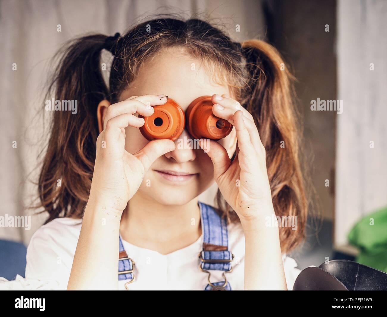 Nettes kleines Mädchen hat Spaß mit Blumentöpfen als Schutzbrille. Kinderunterhaltungen, glückliche Momente. kaukasische Ethnie. Nahaufnahme Stockfoto