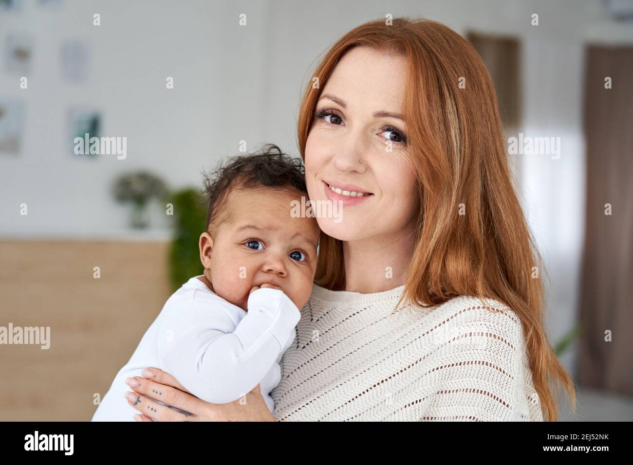 Glücklich junge kaukasische Mutter hält niedlich afrikanisch amerikanisch Baby Tochter. Hochformat Stockfoto
