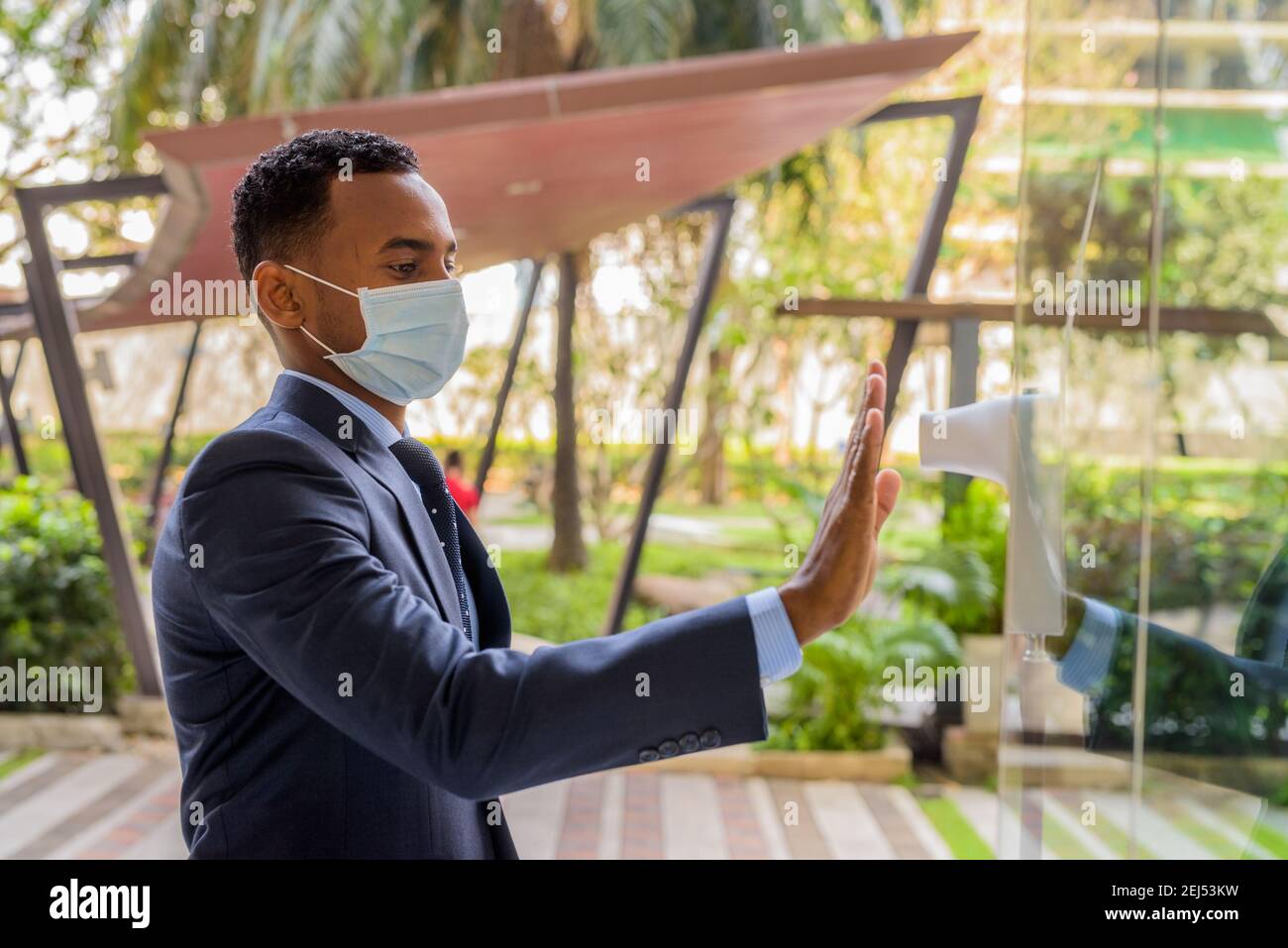 Afrikanischer Geschäftsmann mit chirurgischer medizinischer Maske für Schutz messenden Körper Temperatur vor dem Betreten des Gebäudes Stockfoto