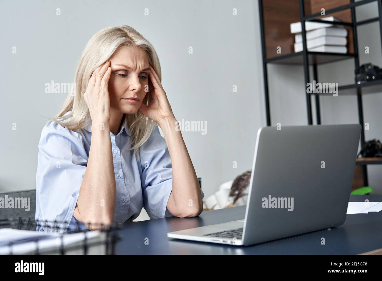 Gestresste alte Geschäftsfrau, die nach der Computerarbeit unter Kopfschmerzen leidet. Stockfoto