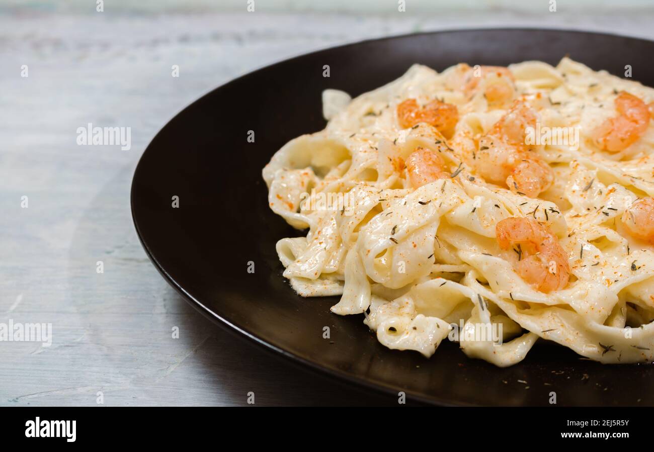 Köstliche italienische Pasta. Fetuccini mit Garnelen und Kräutersauce auf schwarzem Teller. Stockfoto