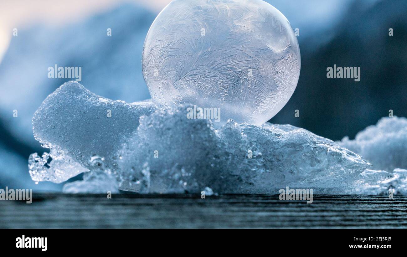 Schöne gefrorene Blasen sitzen auf einem Haufen von Schnee und Eis mit einer zarten Struktur von Eisblumen beleuchtet Die aufgehende Sonne mit Bergen im Hintergrund Stockfoto