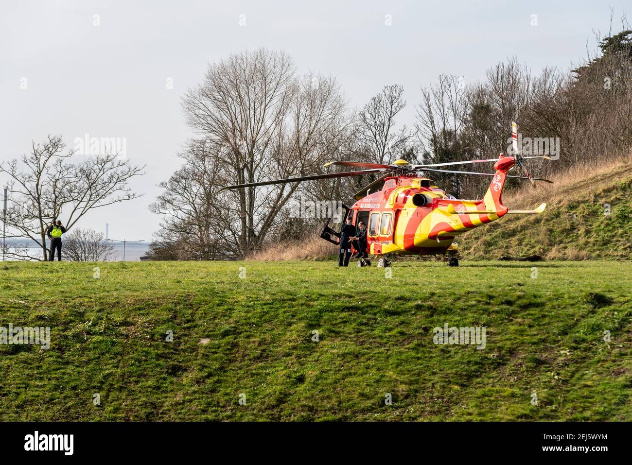 Essex & Herts Air Ambulance landete an einem sonnigen Tag auf Klippen in Southend on Sea, Essex, Großbritannien. Crew wartet mit dem Hubschrauber. Ziviler Patrouillenoffizier Stockfoto