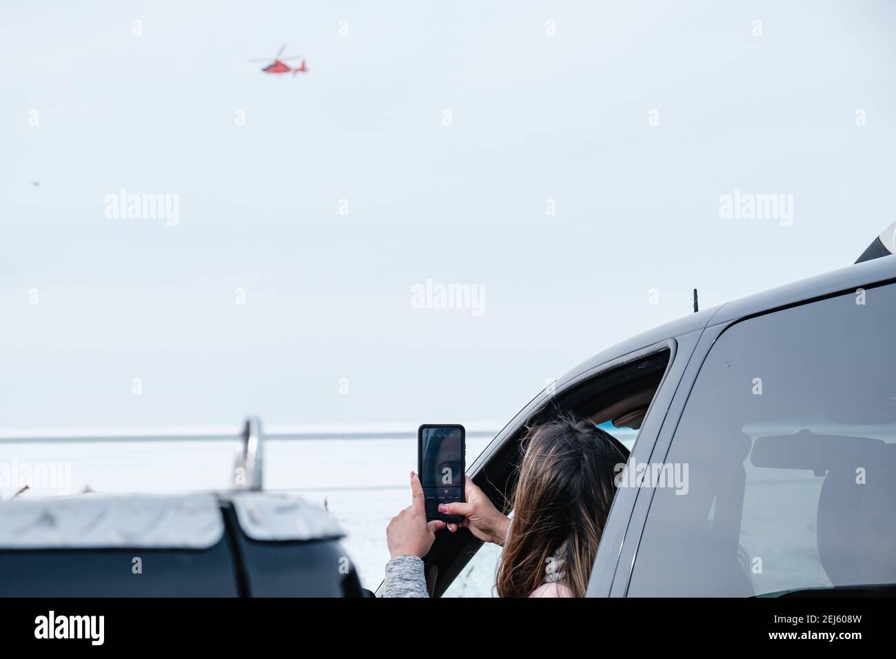 Cleveland, Ohio, USA. Februar 2021, 21st. Eine Frau fotografiert einen Hubschrauber der US-Küstenwache, während Menschen von Mitgliedern des USCG Ice Rescue Teams von Station Cleveland, sowie anderen lokalen Rettungsdiensten, am späten Sonntagnachmittag, 21. Februar 2021 im Edgewater Park in Cleveland, Ohio, vor dem Eis des Eriesees gerettet werden. Um 12:43 EST gibt der National Weather Service in Cleveland eine Warnung aus, nicht auf das Eis zu gehen, da sich signifikante Risse durch Südwinde entwickeln. Laut einem Tweet vom USCG Great Lake rettete das '''¦ USCG-Eisrettungsteam 6 Personen über das Eis Stockfoto