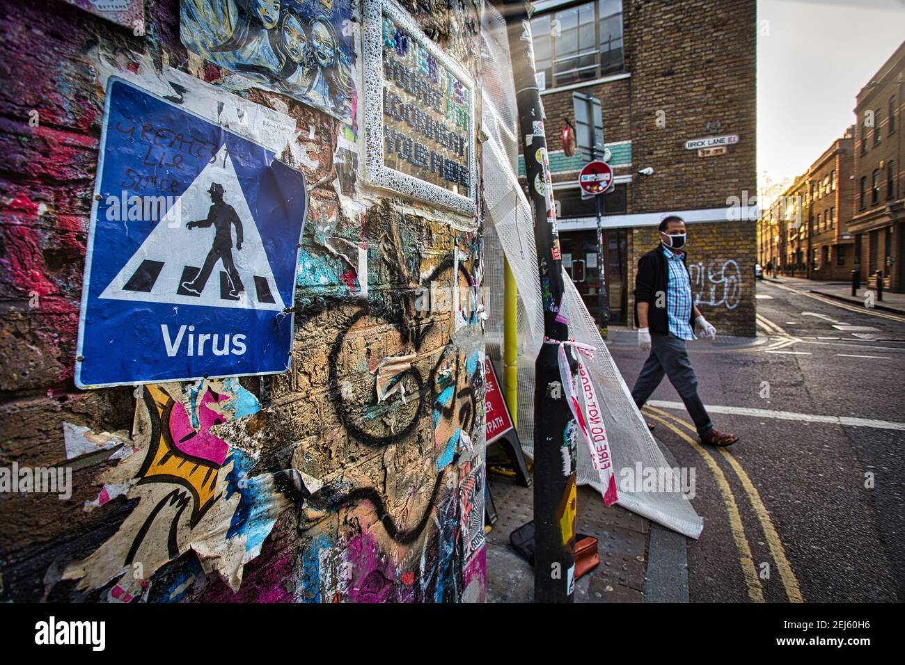 GROSSBRITANNIEN / England / London / EIN Mann mit Gesichtsmaske kommt an der Covid-19 Street Art vorbei, in der Nähe der Brick Lane in London. Stockfoto