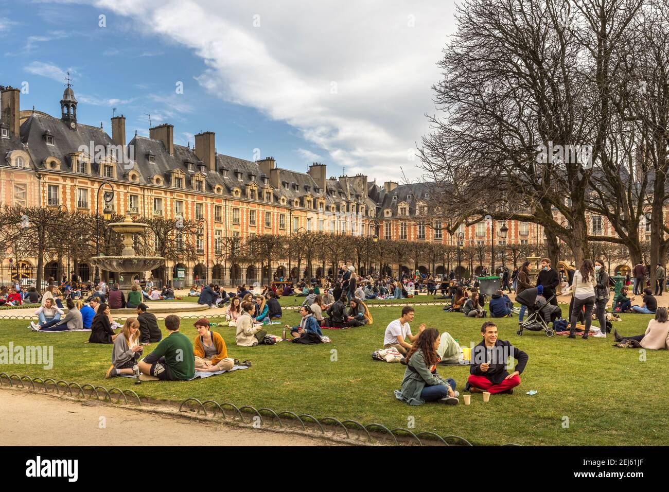 Paris, Frankreich - 21. Februar 2021: Menschen entspannen auf grünen Rasen des berühmten Place des Vosges - älteste geplante Platz in Paris, während covid-19 pandemi Stockfoto