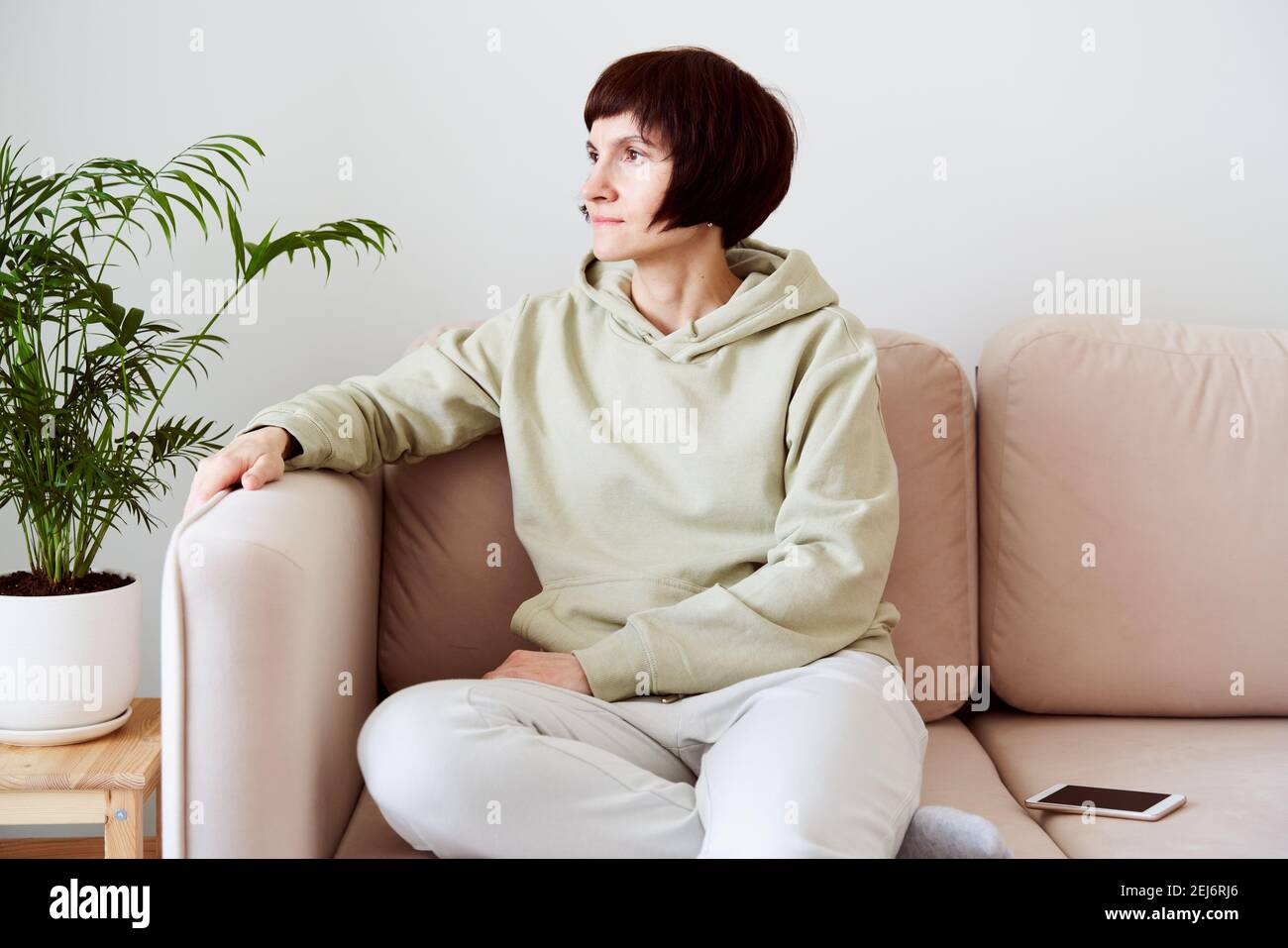Reife Frau verbringt Zeit zu Hause, sitzt im Zimmer auf der Couch und sieht traurig aus. Digitales Detox-Konzept Stockfoto