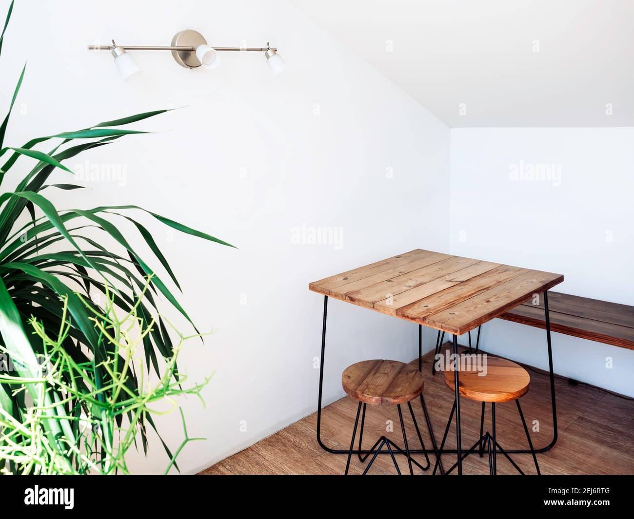 Leerer Holztisch mit runden Stühlen auf Holzboden mit Wandlampe Dekoration in der Ecke des weißen Raumes in der Nähe der grünen Pflanze. Stockfoto