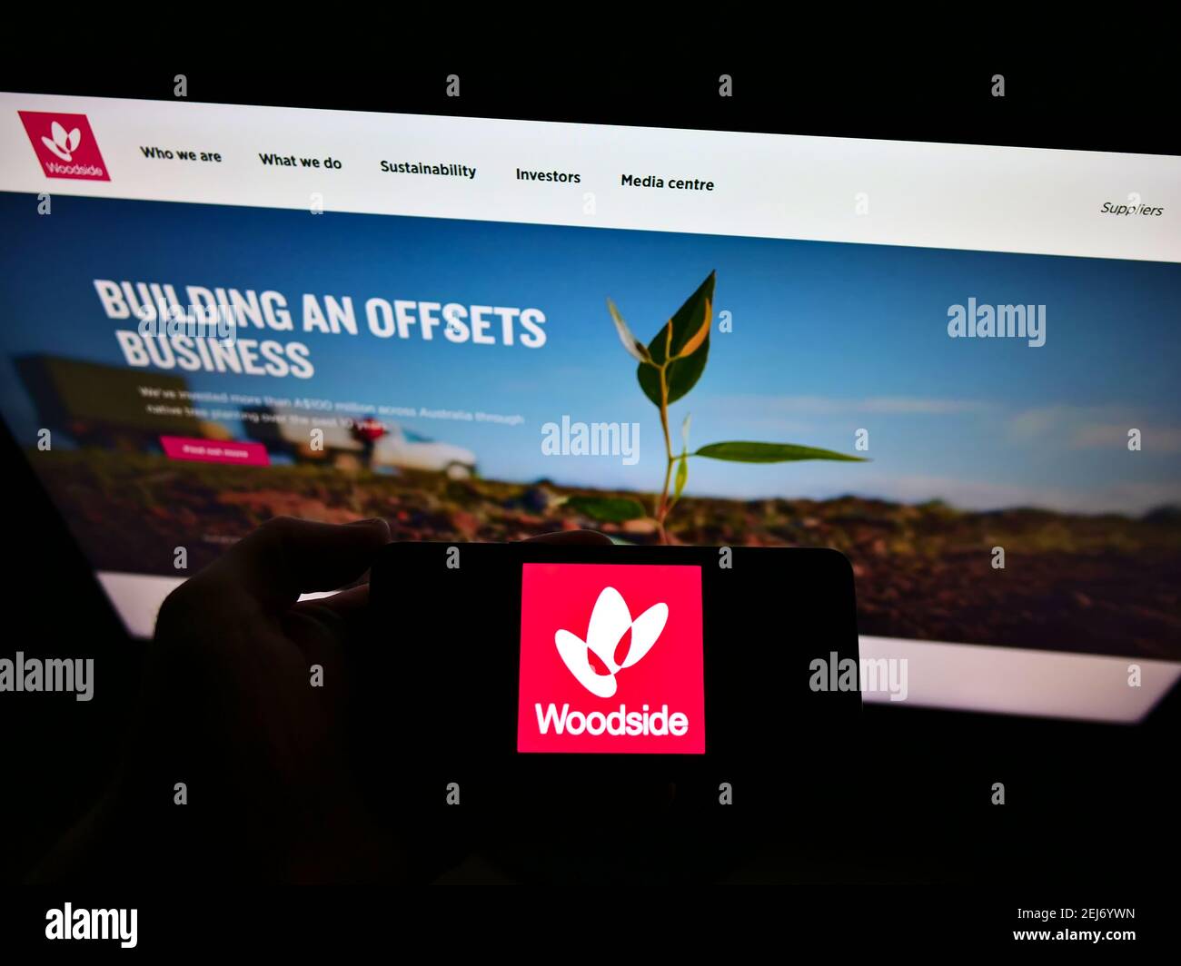Person hält Handy mit Logo der australischen Ölgesellschaft Woodside Petroleum Ltd auf dem Bildschirm vor der Webseite. Fokus auf Handy-Display. Stockfoto