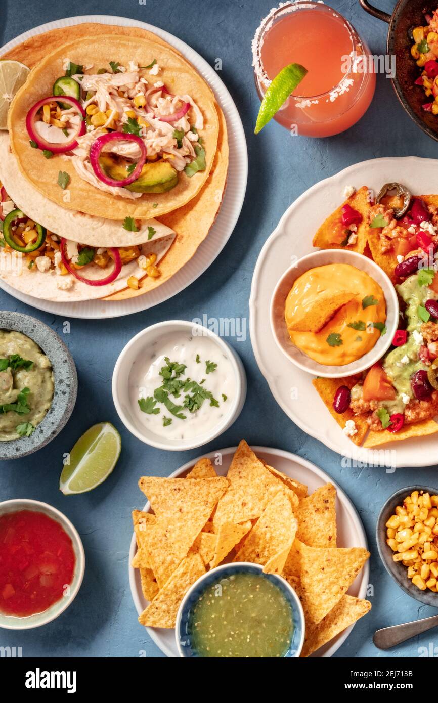 Mexikanisches Essen auf blauem Hintergrund. Nachos, Tacos und Dips, Cocktails, Overhead Shot Stockfoto