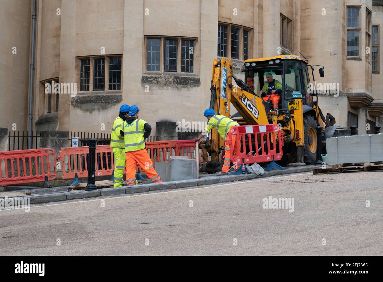 Reparaturarbeiten auf städtischen Bürgersteig, Bagger und Arbeiter in Sichtbekleidung arbeiten auf der Straße Stockfoto