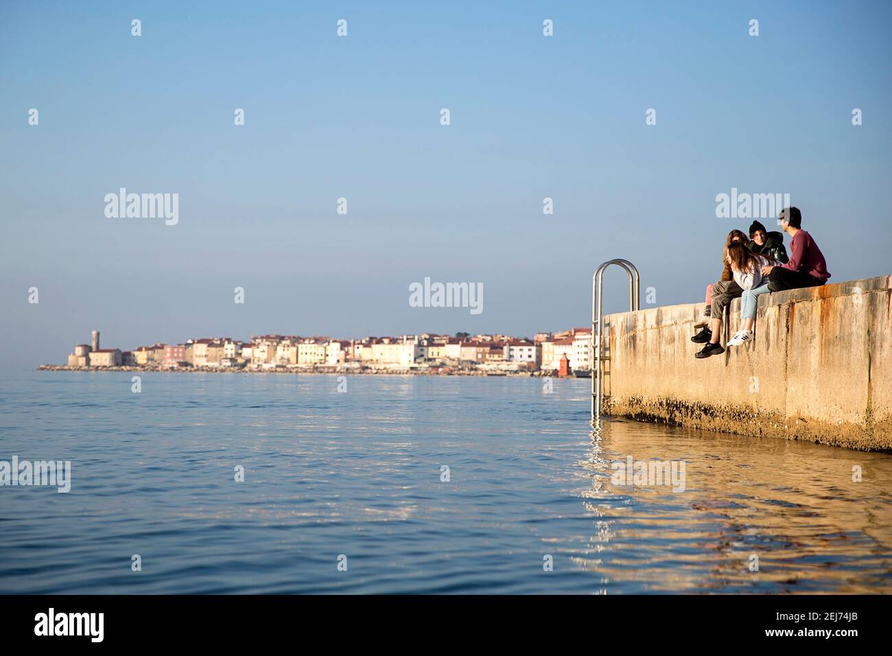 Gruppe von jungen Menschen hängen an einem Betonsteg, malerische Altstadt Piran an der slowenischen adriaküste im Hintergrund, Slowenien, Europa Stockfoto