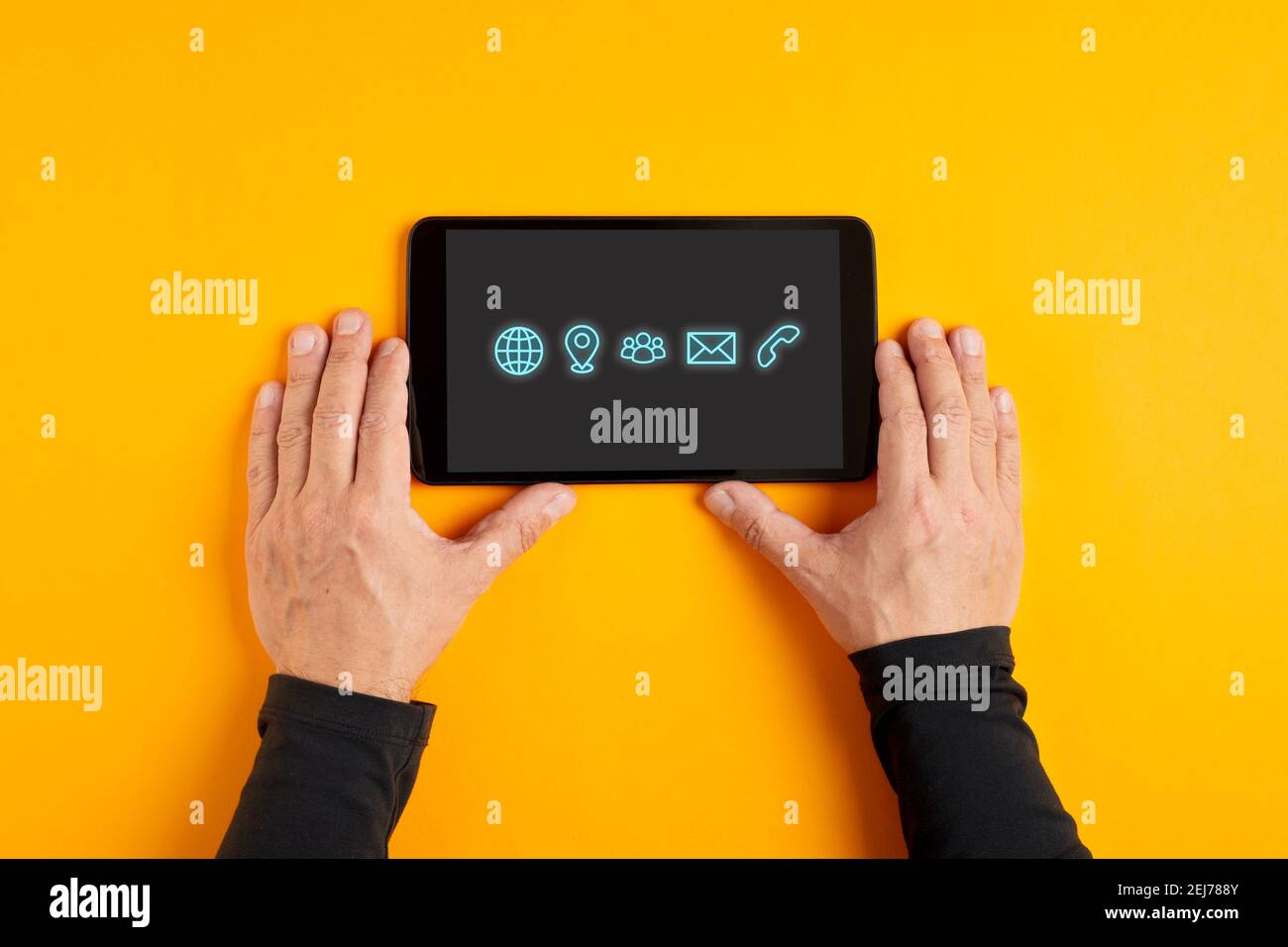 Männliche Hand mit einem schwarzen digitalen Tablet, das Kontaktsymbole und Kommunikationssymbole auf gelbem Hintergrund anzeigt. Stockfoto