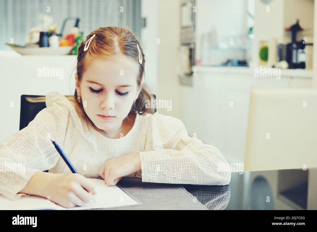 Weiß kaukasische Mädchen (Kind, Kid) Platzierung auf einem Tisch und Schreiben in einem Notebook. Studieren. Stockfoto