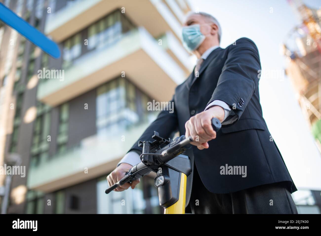 Maskierter Geschäftsmann mit seinem Elektroroller, covid Coronavirus Ökologie Mobilität und Verkehr Konzept Stockfoto