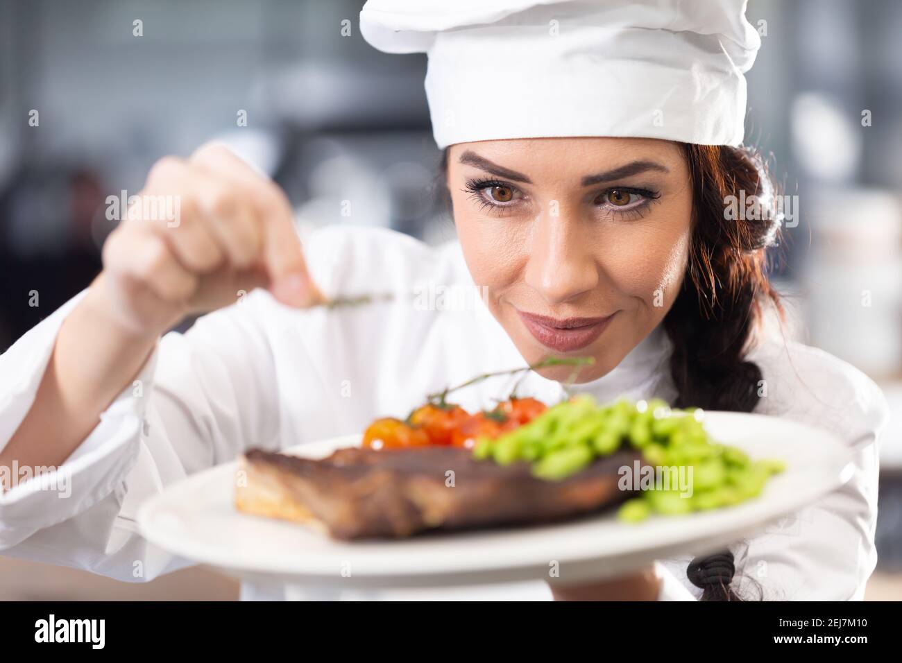 Professionelle Köchin im Hut macht den letzten Schliff auf einem frisch zubereiteten Steak vor dem Servieren. Stockfoto