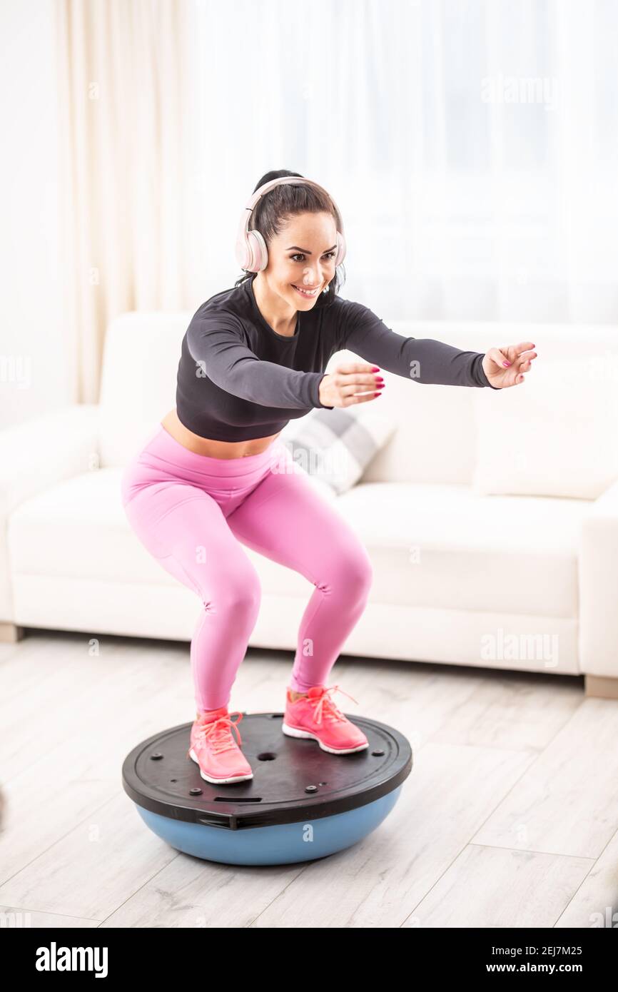 Passen Sie schöne Frau in ein Trainingsoutfit und Kopfhörer auf Kniebeugen auf einem Balance Ball. Stockfoto