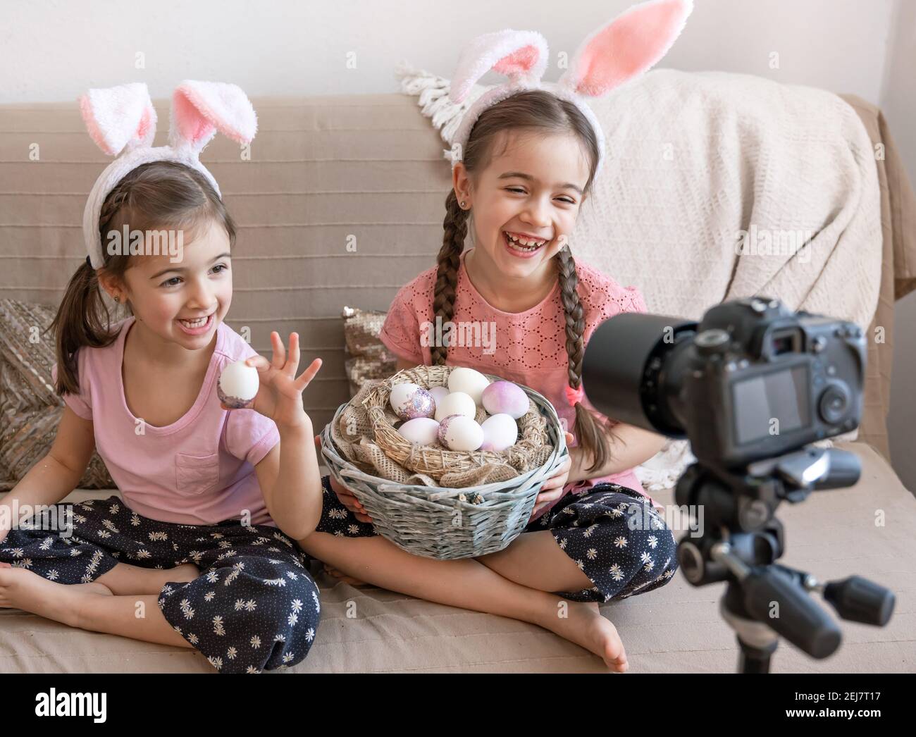 Kleine glückliche Schwestern mit Hasenohren posieren für die Kamera mit einem Korb mit Ostereiern. Ostern Foto Session Konzept. Stockfoto