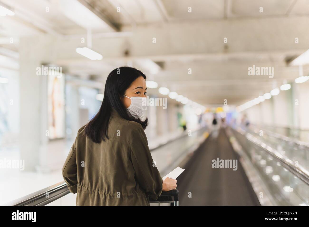 Frau mit Bordkarte, die auf der Rolltreppe mit Trolley läuft. Stockfoto