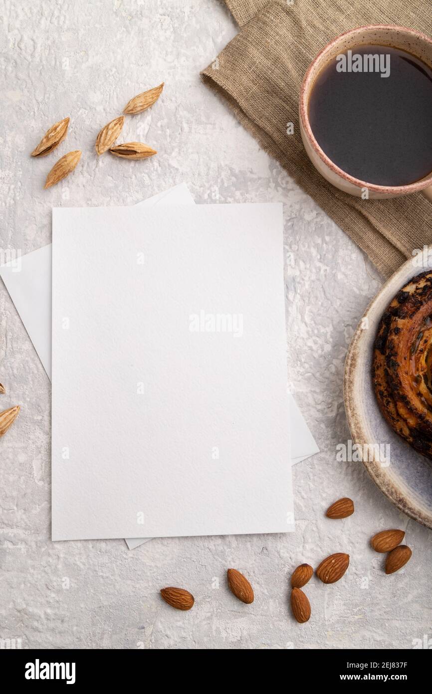 Weißes Papier Einladungskarte, Mockup mit Mandeln, Brötchen, Tasse Kaffee, Leinentextilien auf grauem Betongrund. Blank, flach liegend, Draufsicht, Stillleben Stockfoto