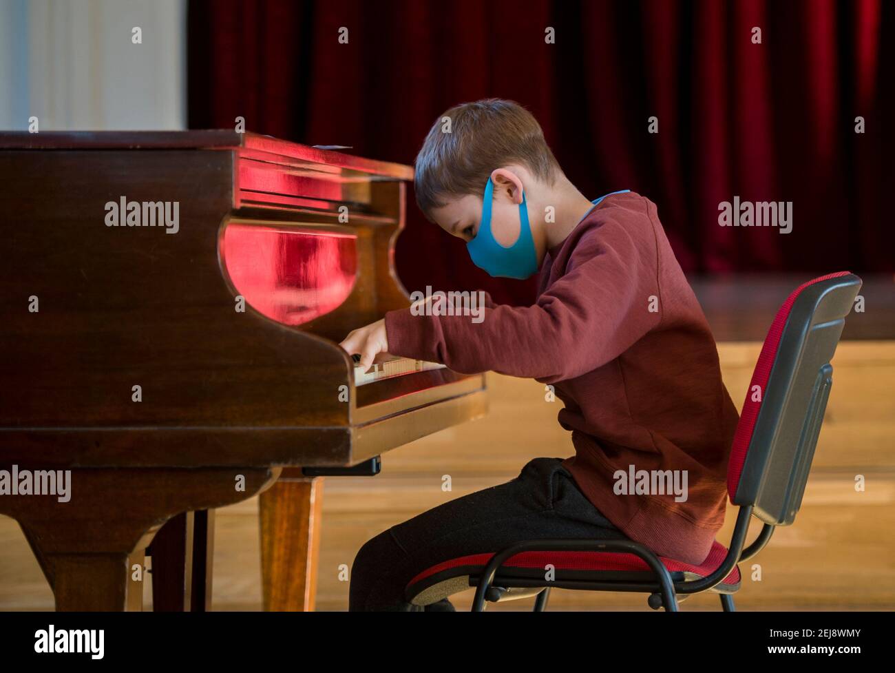 Junge mit blauer Maske und Klavierspiel bei Unterricht und Veranstaltung. Kinder zurück zur Schule Konzept Stockfoto