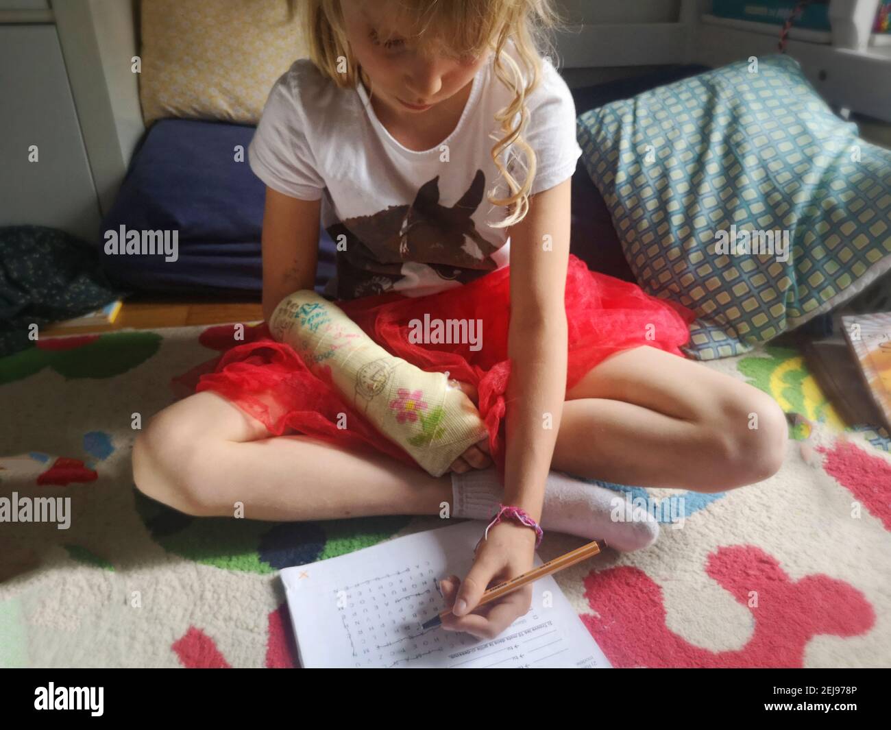 7-9 Jahre altes europäisches Mädchen mit einem verputzten gebrochenen Arm, das ihre Hausaufgaben mit ihrer linken Hand macht, Frankreich. Stockfoto